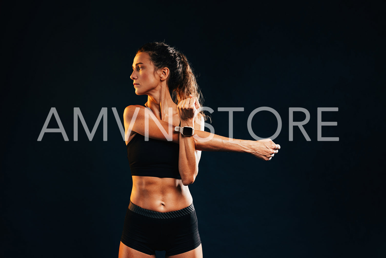 Young muscular woman stretching her arm in studio on black background looking away