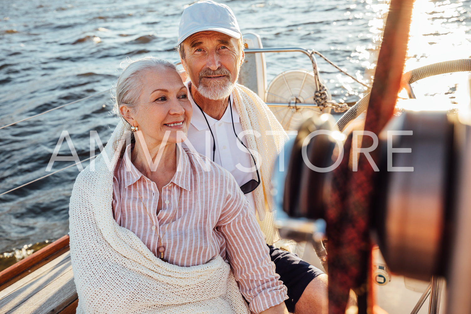 Mature couple sitting on yacht and wrapped in a white blanket	