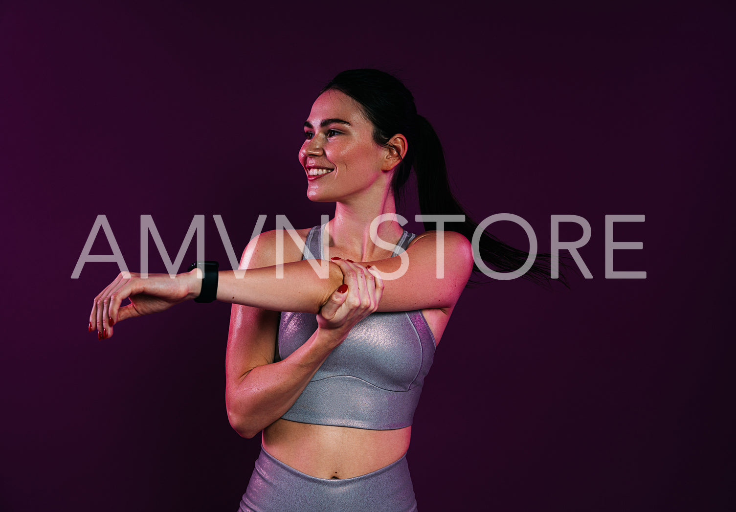 Smiling slim female flexing her hand against a magenta background in studio