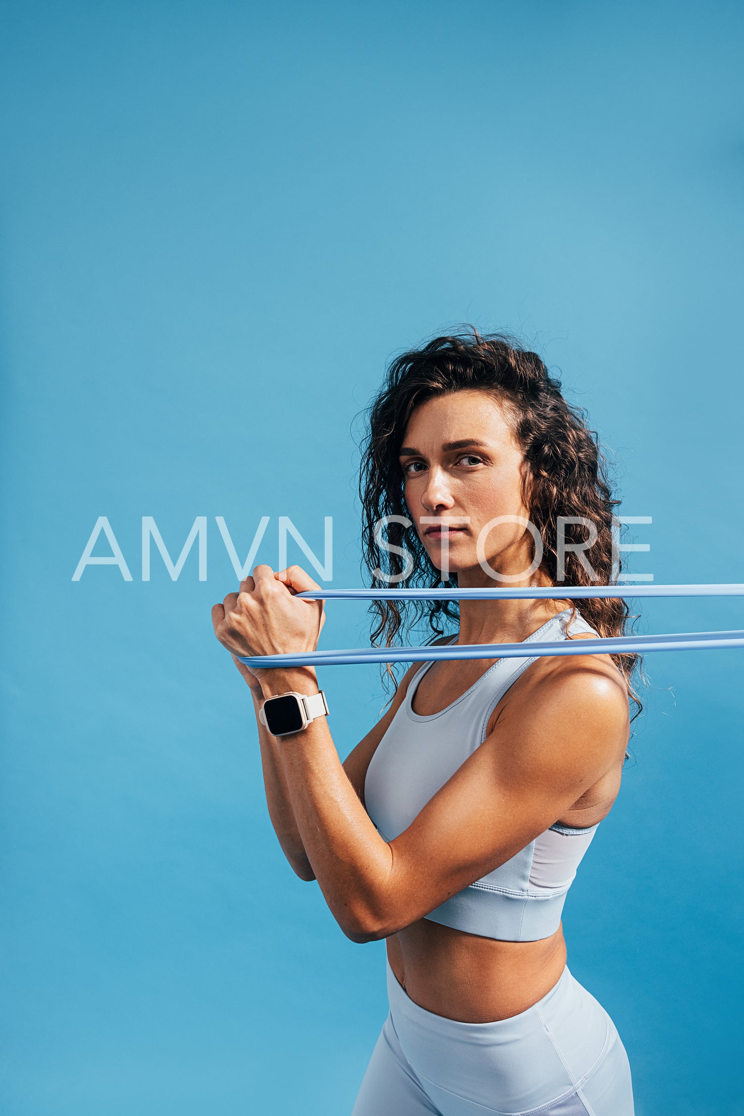 Sportswoman working out with elastic band on blue background background and looking at camera