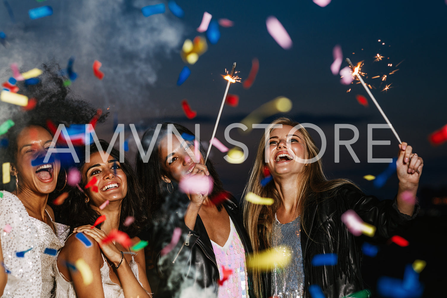 Four happy girls celebrating at night under colorful confetti holding sparkles and laughing	