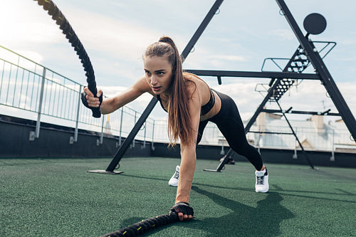 Muscular woman working out with battle ropes on rooftop terrace