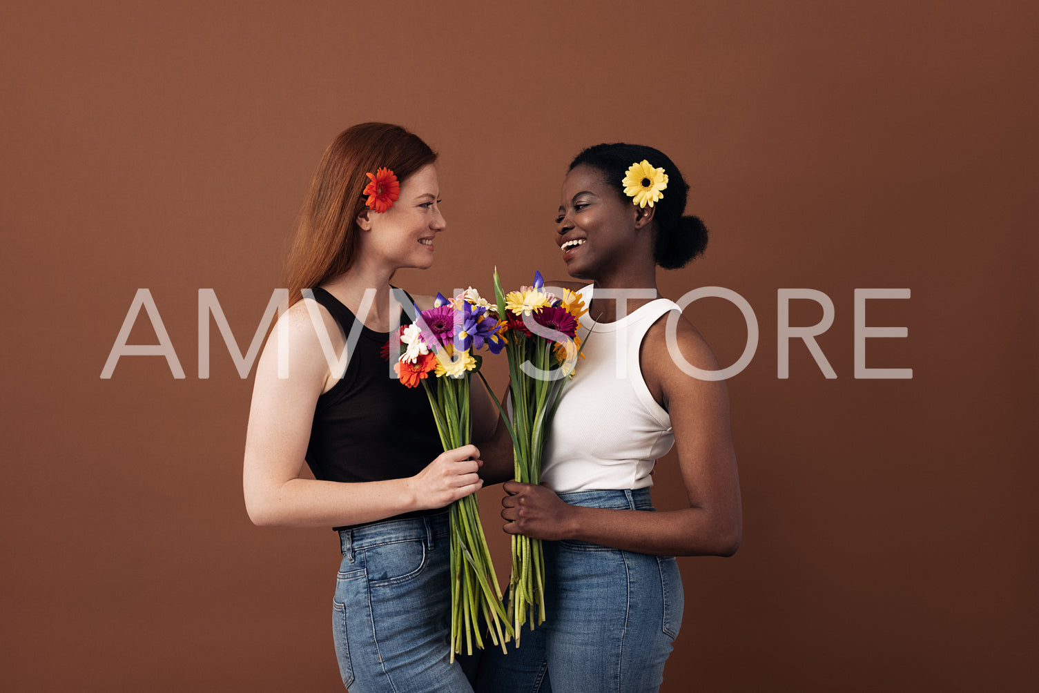 Two women of different races holding bouquets of flowers looking at each other in a studio