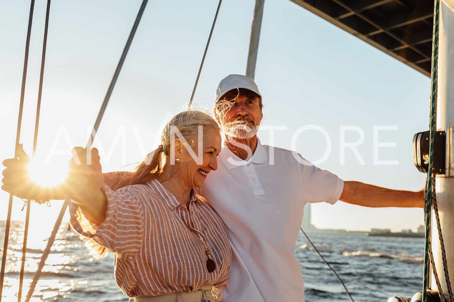 Elderly couple enjoying their vacation on a private yacht. Two senior people standing together on a sailboat at sunset.	