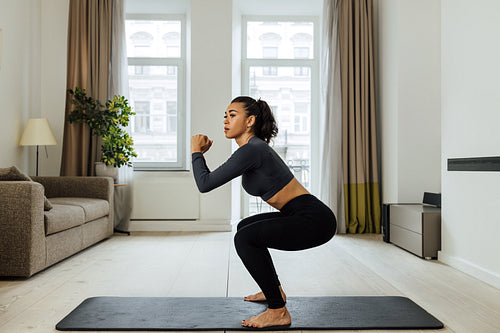 Side view of a fit woman doing sit-ups on mat in living room