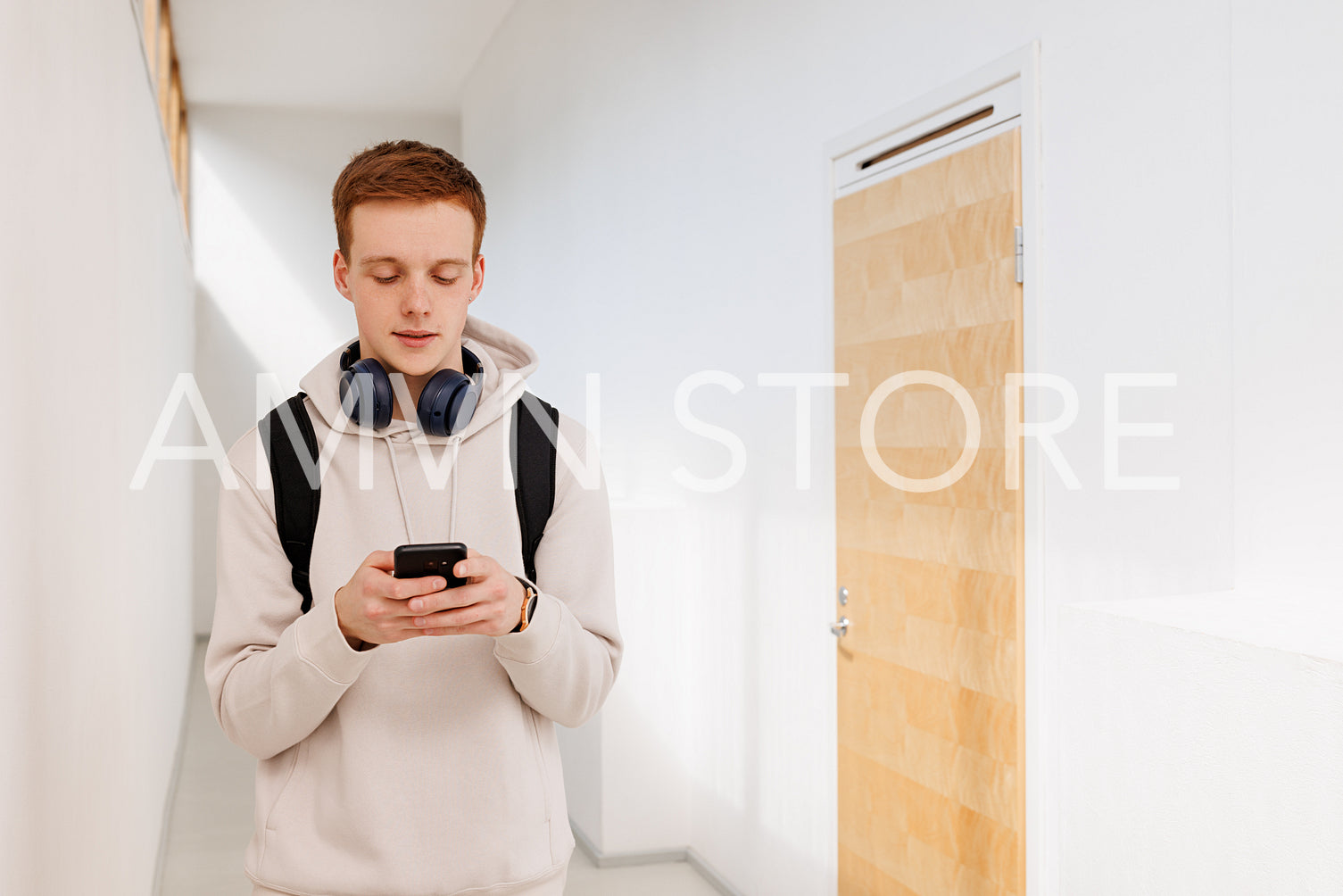 Male student walking in the corridor and using a smartphone