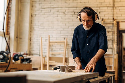 Senior carpenter in noise cancelling headphones working on saw machine