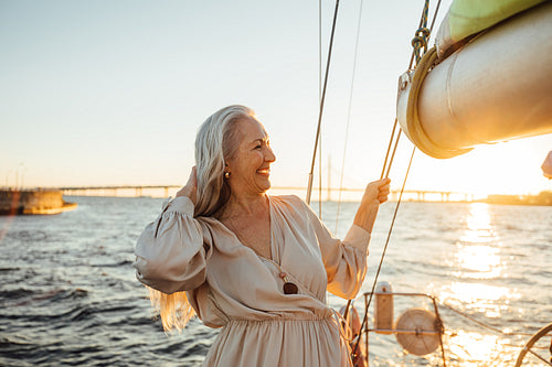 Side view of a beautiful senior woman adjusting her hair and enjoying sunset on private yacht