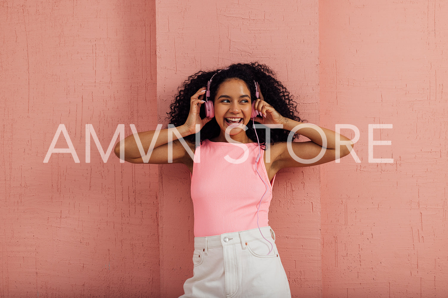 Beautiful woman with curly hair listening to music by pink headphones wearing casual clothes having fun