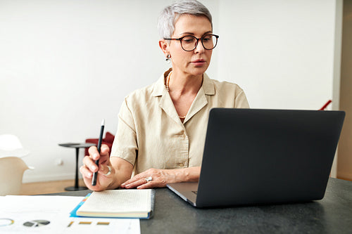 Mature woman looking on laptop screen holding a pen