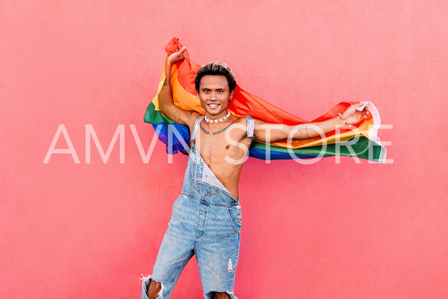 Happy male with LGBT flag standing against pink wall looking at camera