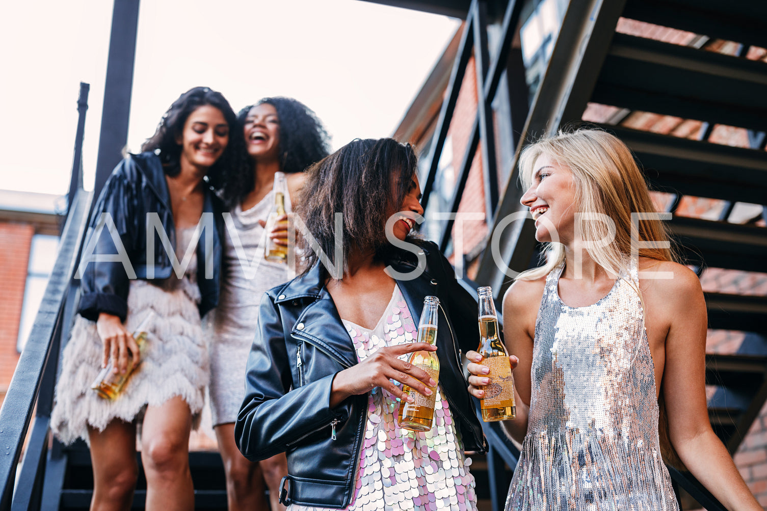 Happy women walking with bottles of beers. Young female friends having fun while stepping down stairs.	