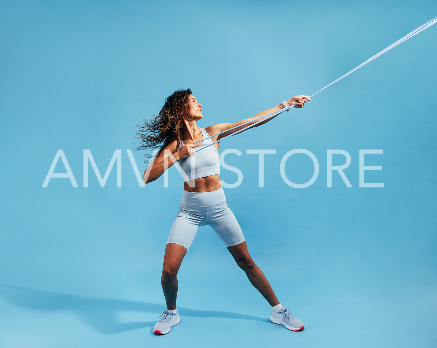 Muscular sportswoman exercising with resistance band on blue background. Female working out with elastic band.