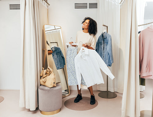 Smiling woman with clothes on hangers having fun in a dressing room