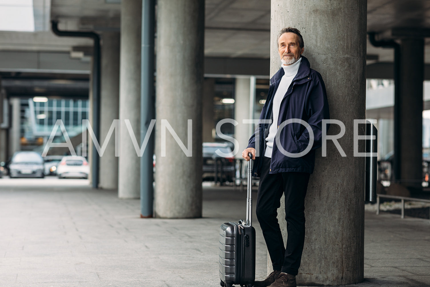 Stylish mature tourist standing outdoors. Man with a suitcase leaning on the wall looking away.	