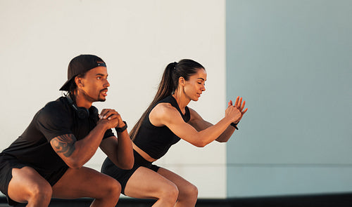 Side view of two athletes ding sit-ups at a wall. Muscular man and woman are training together.