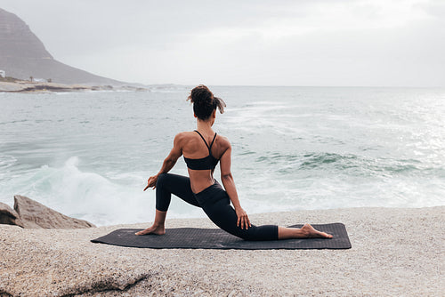 Young woman practicing yoga at evening by ocean. Slim female stretching her body by coast.