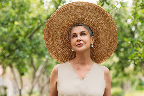 Senior stylish woman in a straw hat standing in the park and looking up