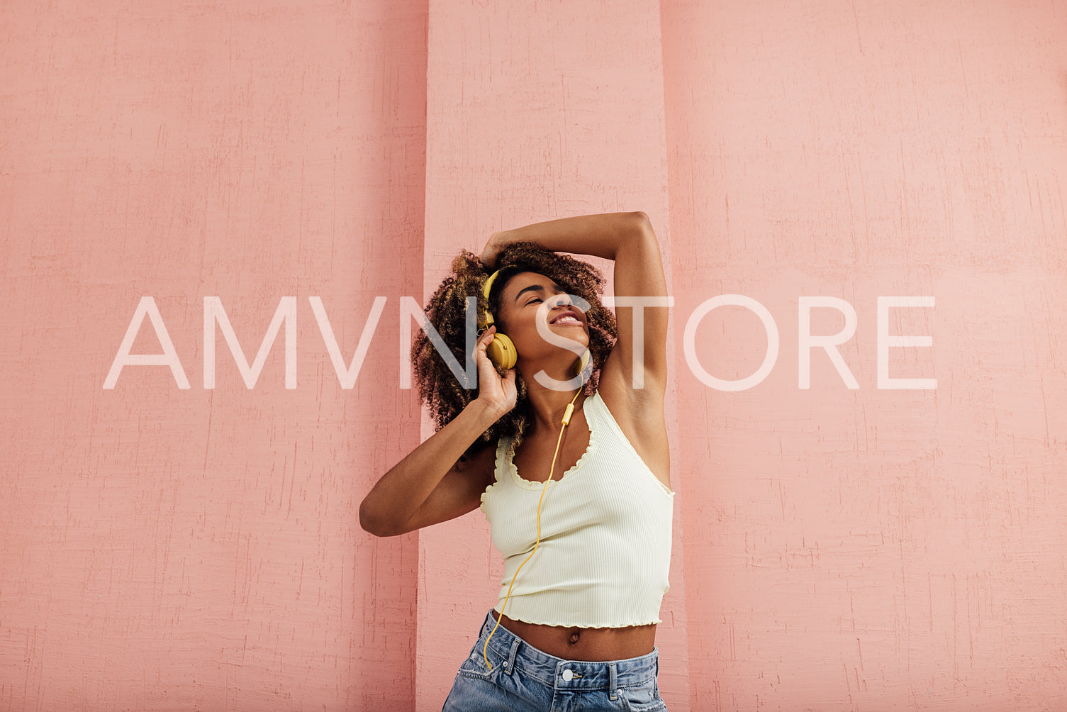 Woman with curly hair enjoying music against pink wall