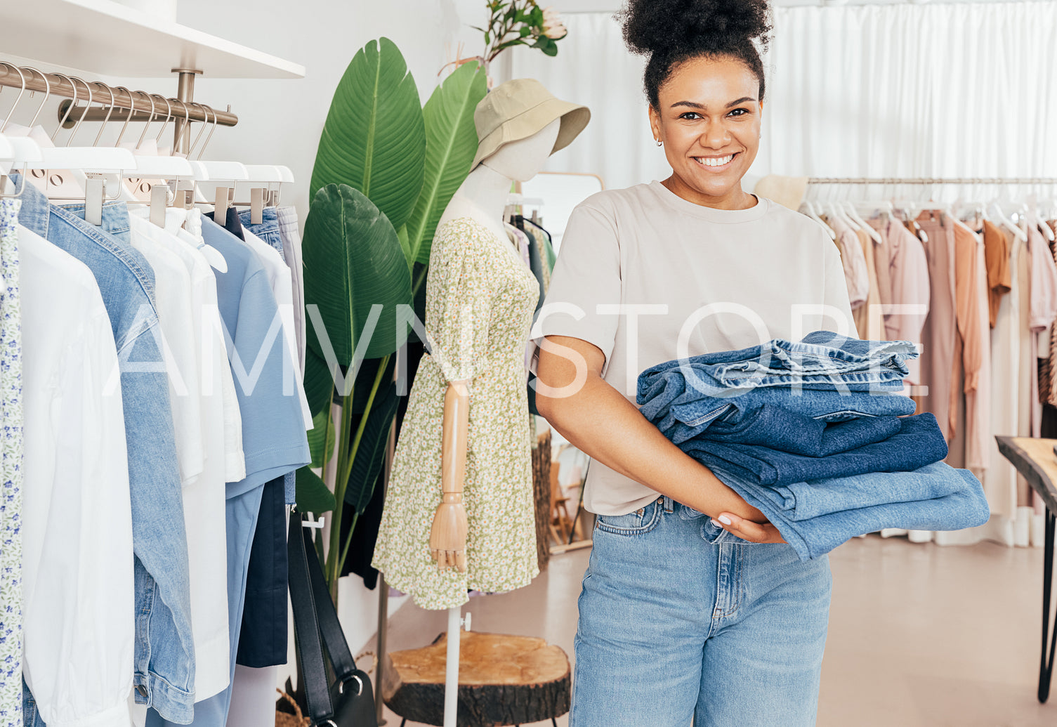 Smiling female fashion store worker holding a pile of jeans and looking at camera