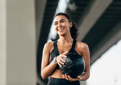 Beautiful woman holds a medicine ball standing under highway relaxing during training