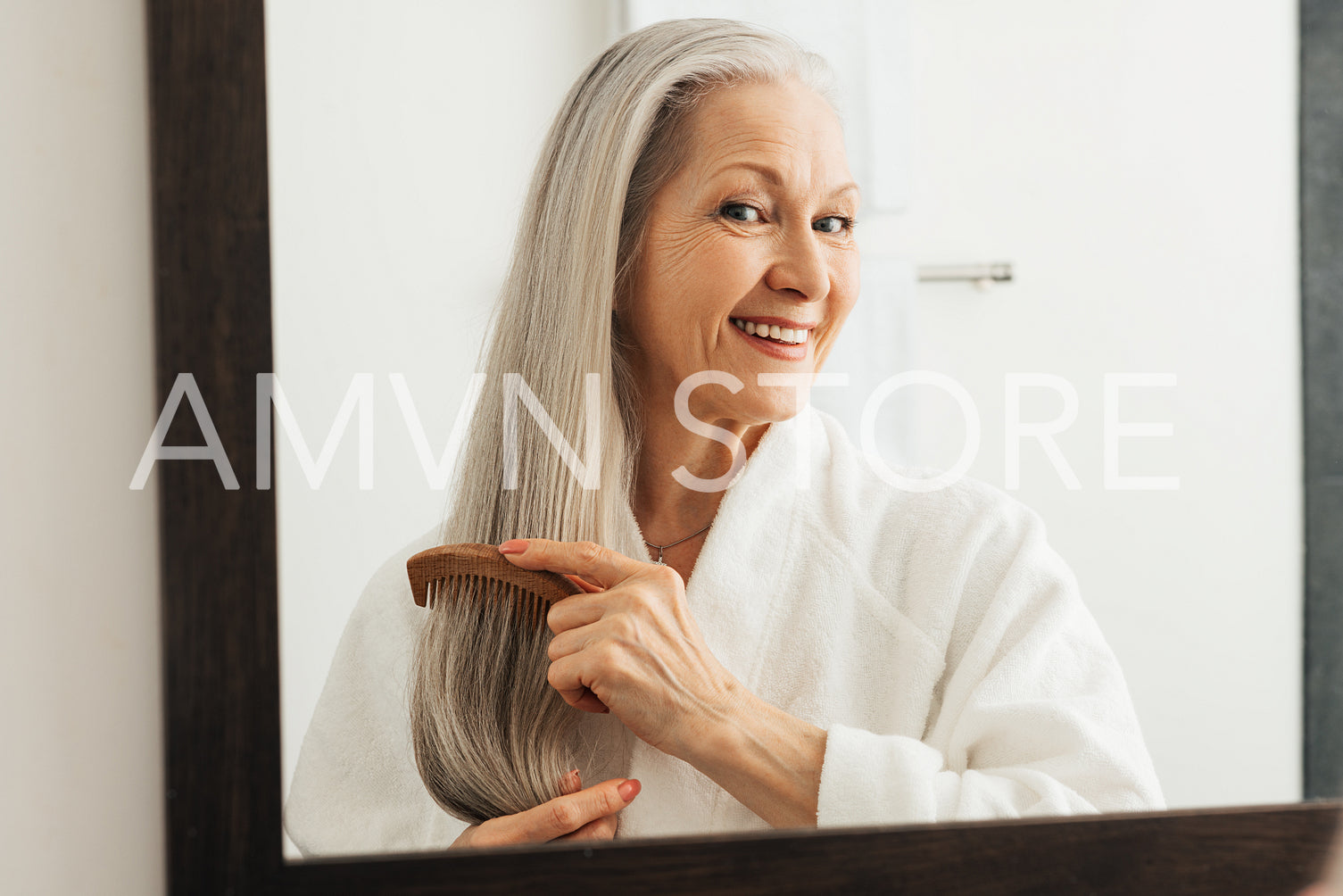 Woman combing her hair in bathroom. Senior female using a wood comb.