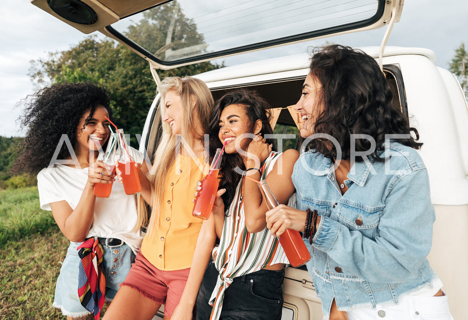 Group of diverse female friends toasting bottles near camper van. Four women enjoying road trip.