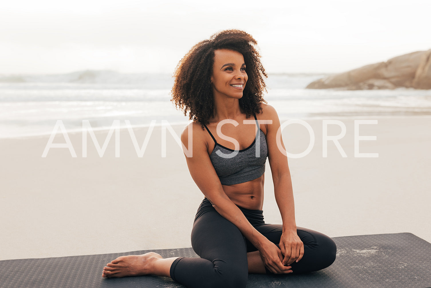 Beautiful smiling woman sitting on mat at beach. Cheerful female relaxing after workout at sunset by ocean.