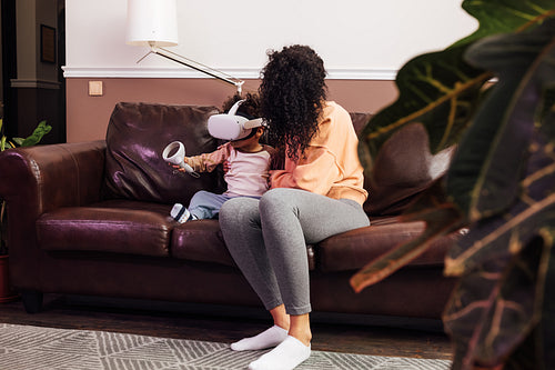 Young mother helping her son while he using VR set on sofa