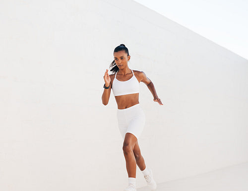 Young jogger running against a white wall outdoors. Muscular woman sprinting.