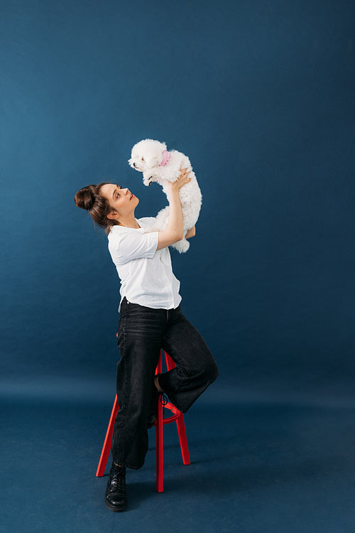 Side view of pet owner lifts up her little white dog against blu