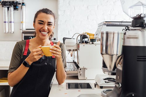 Laughing barista holding a mug. Smiling waitress taking a break in the cafeteria.