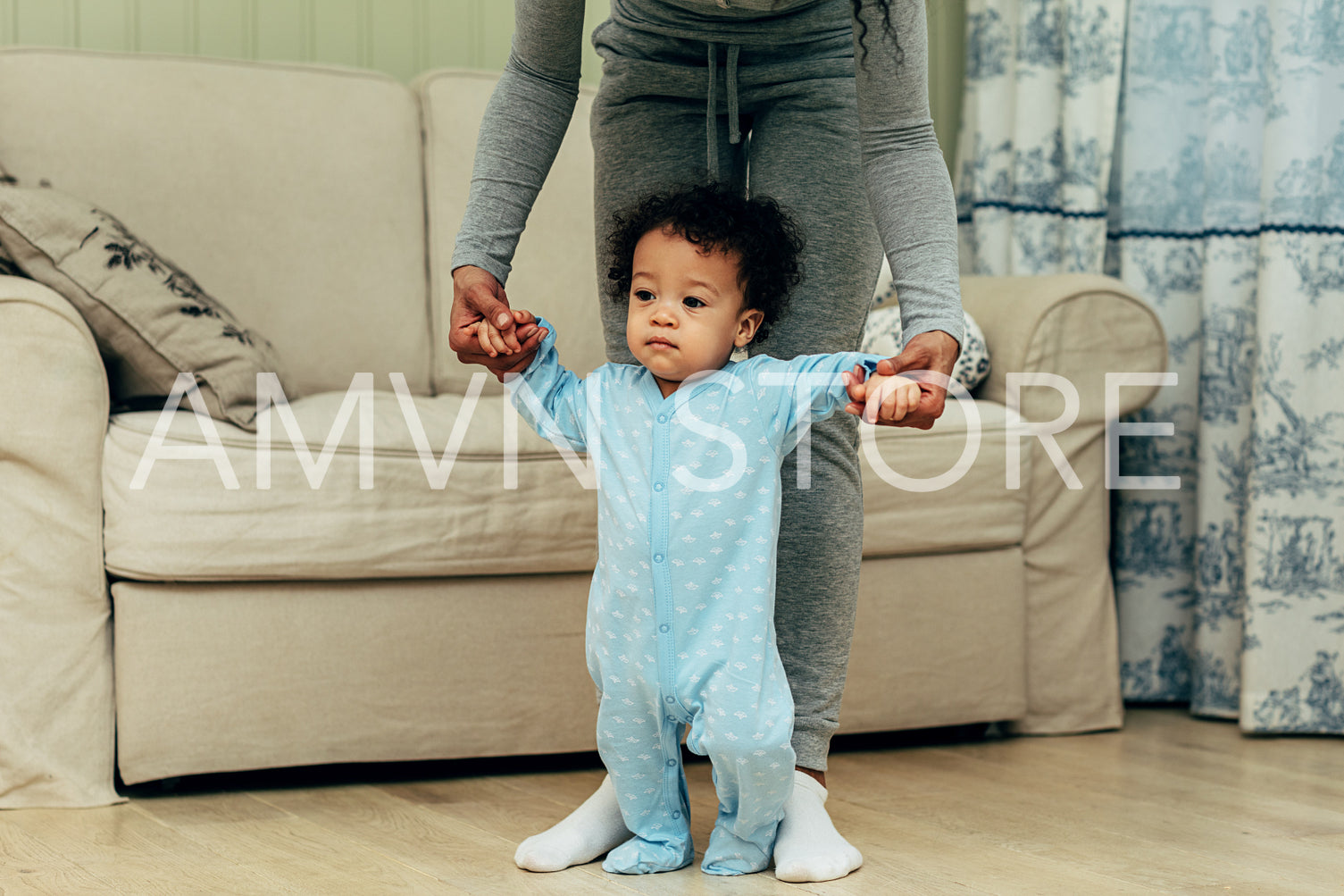 Toddler holding mother's hands in living room. Unrecognizable woman with son.	