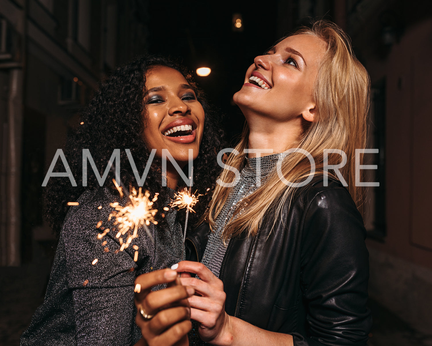 Two happy girlfriends with sparklers laughing outdoors at night	