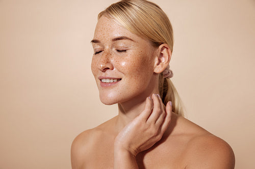 Smiling woman with freckles and perfect skin massaging her neck against pastel background