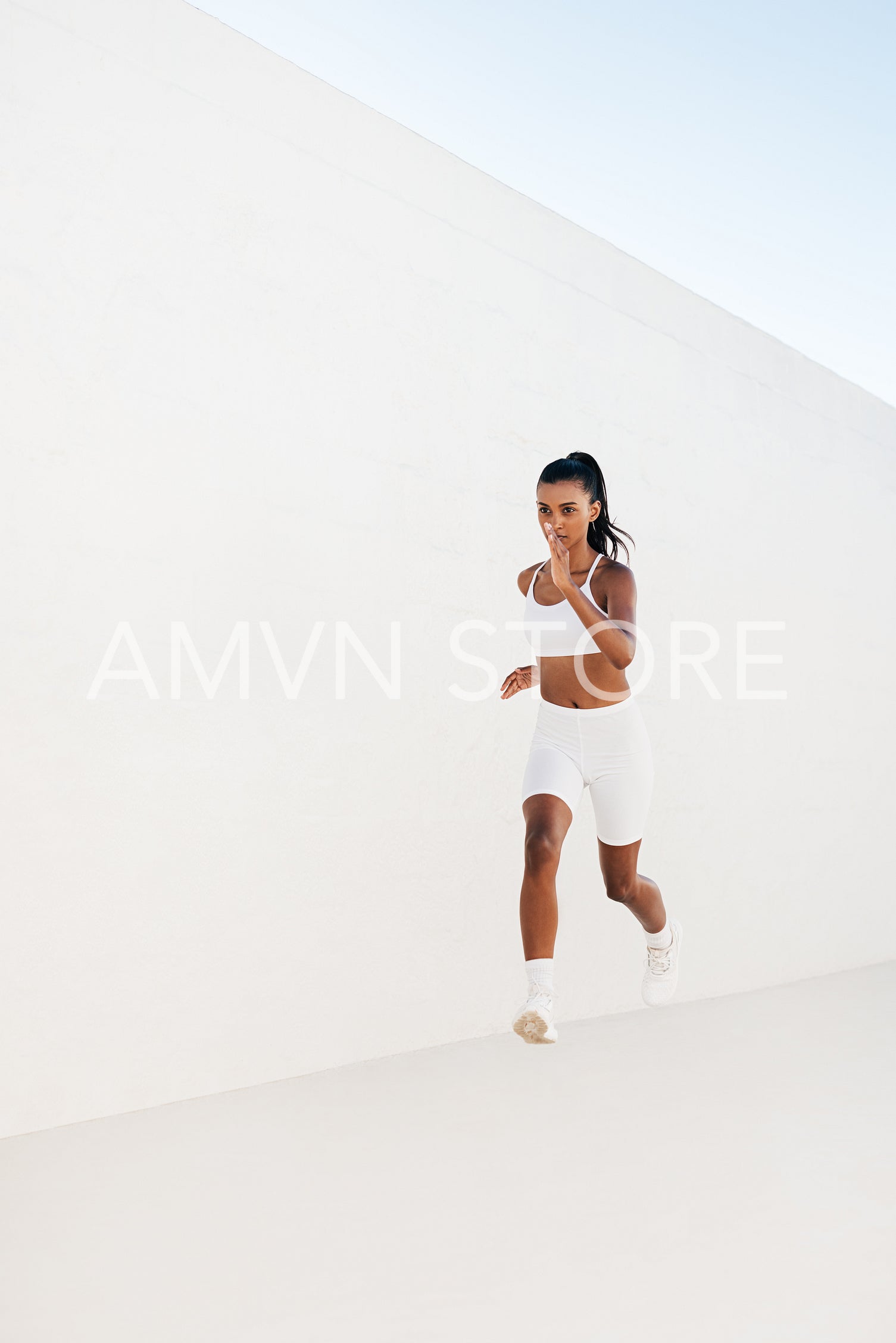 Full length of a slim female sprinting outdoors. Woman jogging outdoors at white wall.