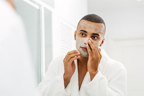 Man looking in the mirror with white clay mask on his face