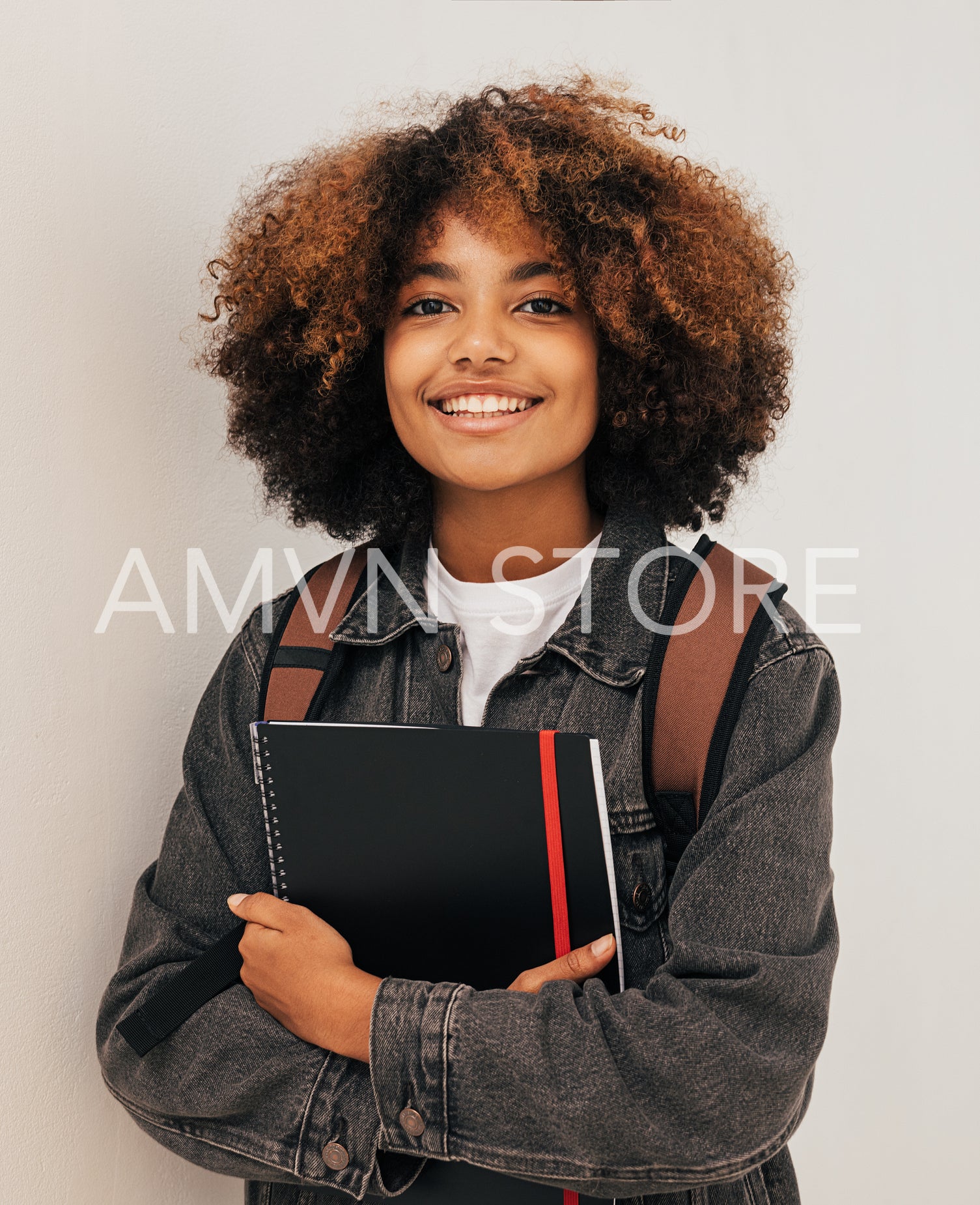 Cheerful girl with curly hair holding a books wearing backpack