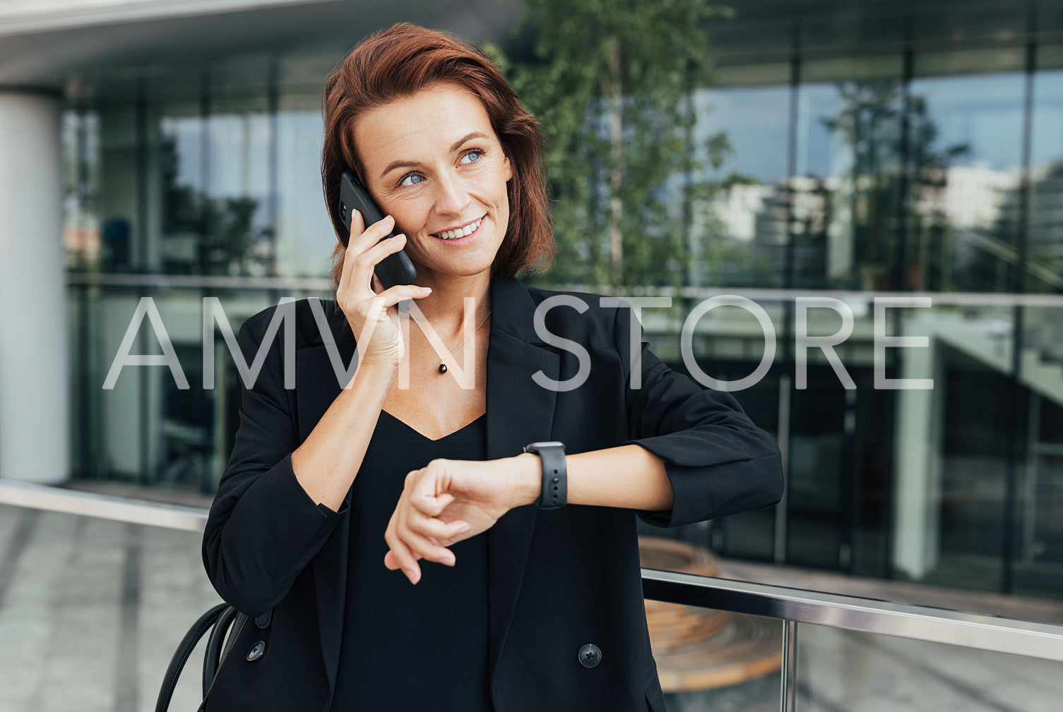 Middle-aged businesswoman talking on mobile phone and looking away. Smiling woman in black formal wear sets a time for a meeting