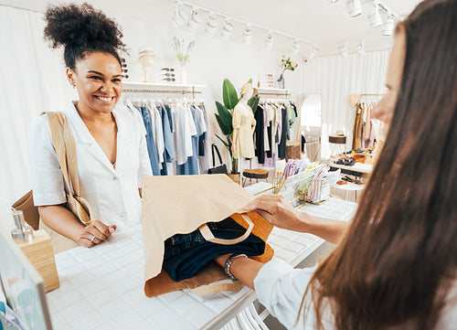 Unrecognizable clothing store owner packing the clothes in a paper bag. Smiling buyer looking at saleswoman while she packing purchase.