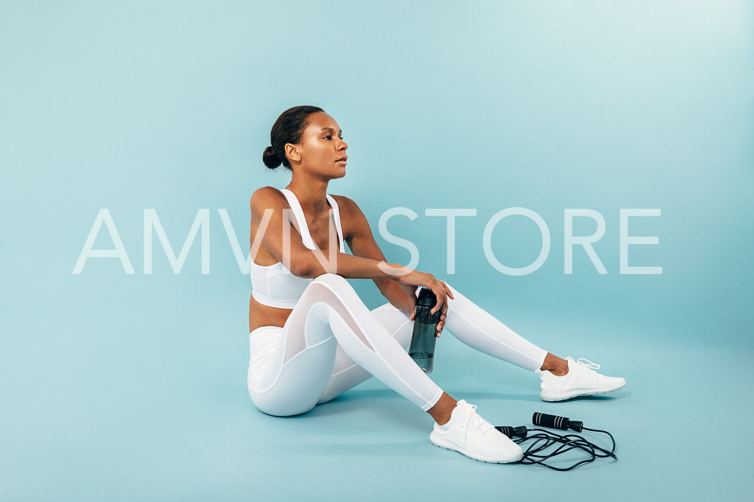 Tired woman in white sportswear sitting on a blue background. Female athlete holding water bottle in studio.	