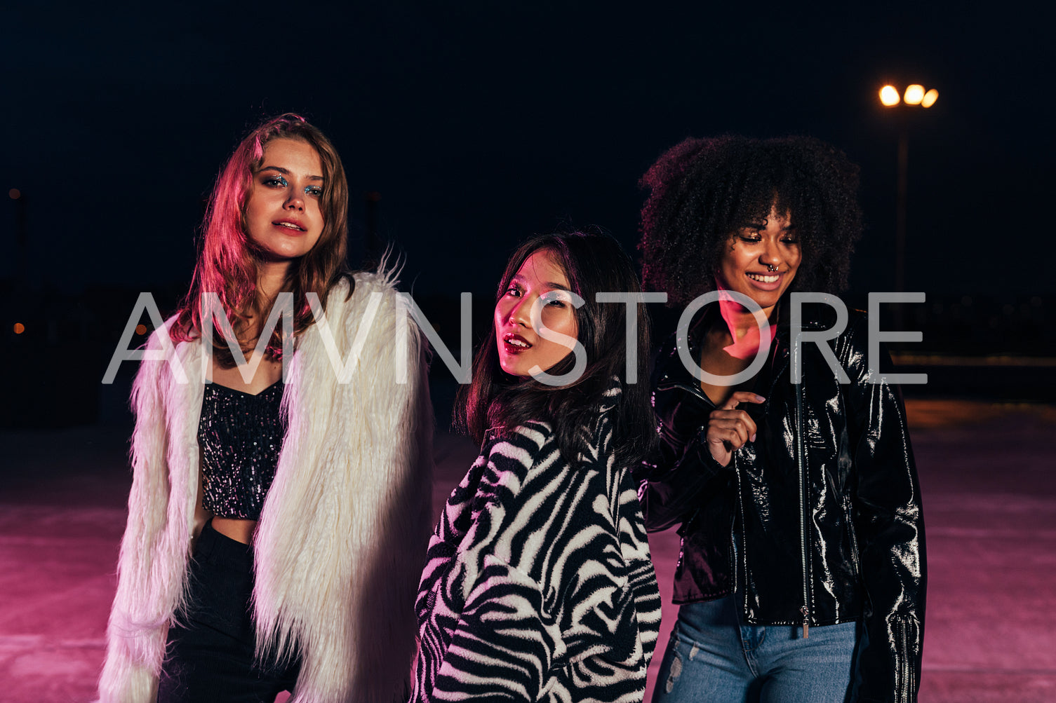 Fashionable girls standing together on roof at night under neon lights. Multi-ethnic group of women posing outdoors and looking at camera.