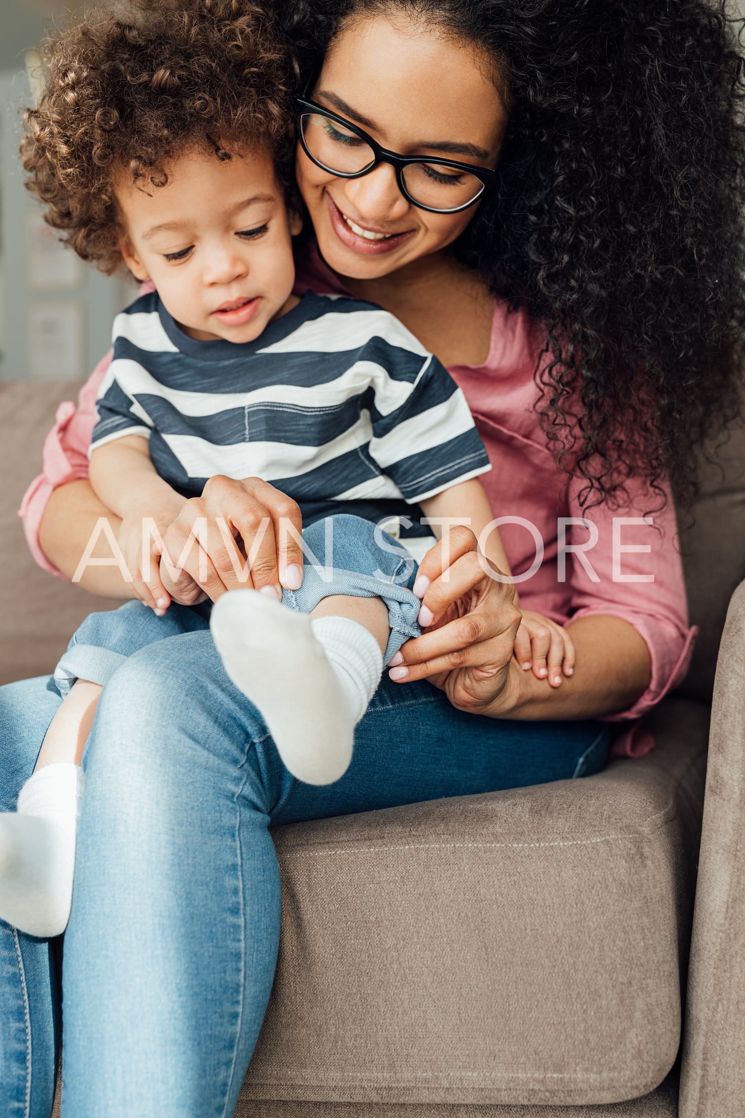 Young mother in eyeglasses helping her son to adjust jeans	