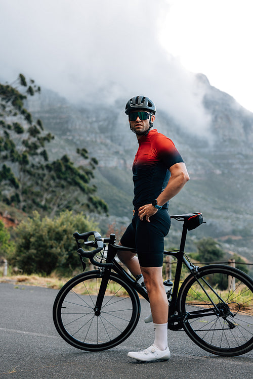 Full length of male cyclist relaxing during training. Professional cyclist standing against a mountain and looking away.