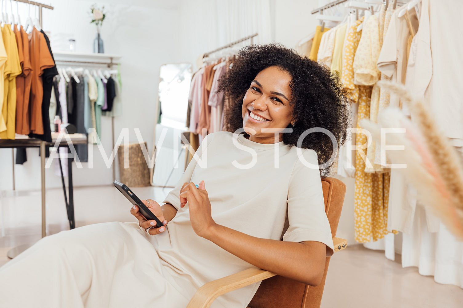 Happy customer sitting in fashion store holding a smartphone and looking at camera