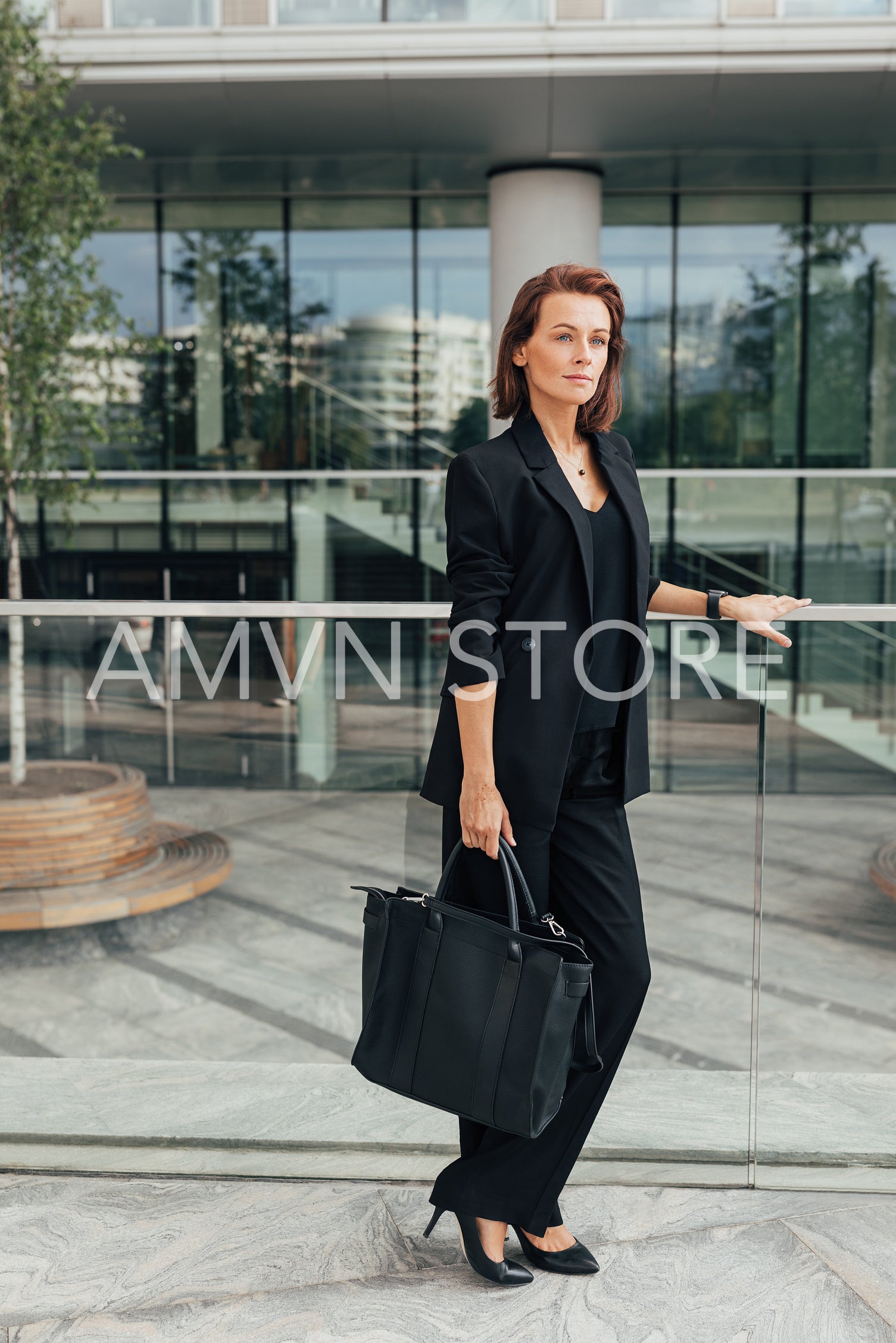 Full length of a middle-aged female in black formal wear leaning a railing standing against office building