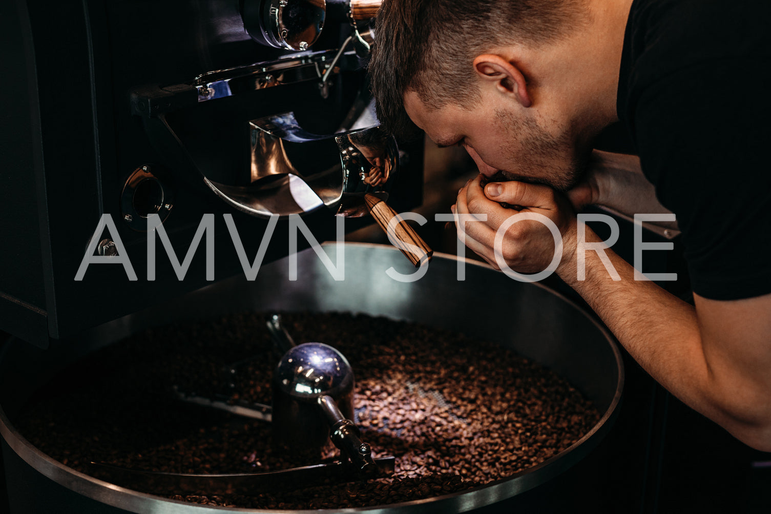 Man smelling coffee beans, standing at roasting machine	