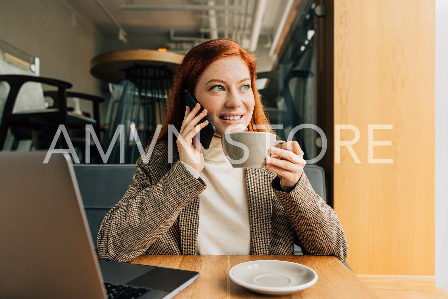 Smiling businesswoman talking on mobile phone and holding a cup of a coffee. Female in formal wear in a cafe.