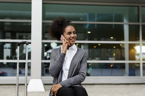 Happy businesswoman sitting at building, talking on mobile phone