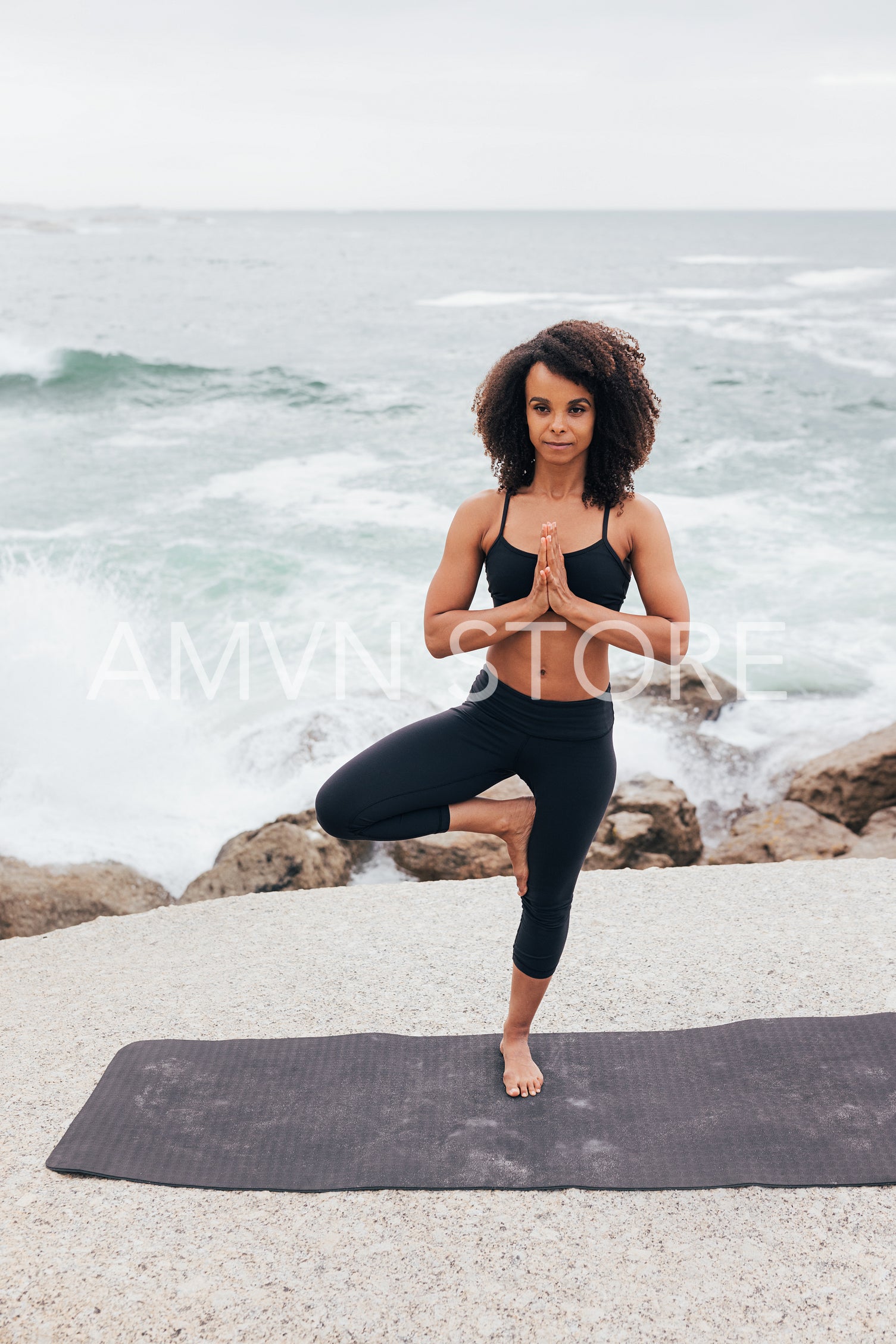 Young woman in Tree pose standing outdoors by ocean